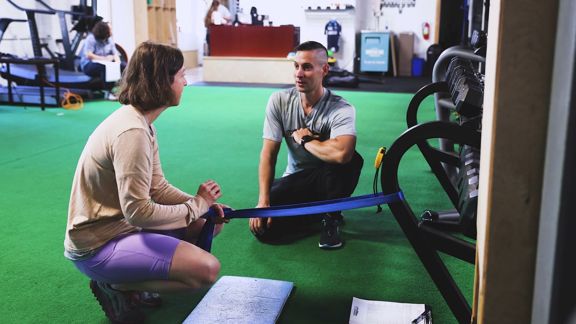 A coach kneeling alongside an athlete working with a resistance band