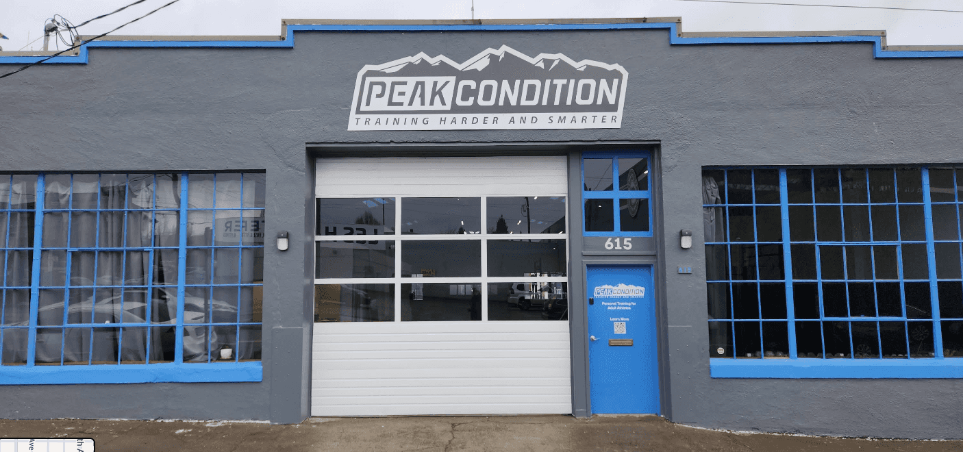 The Peak Condition studio at 615 SE Clay Street, Portland: grey building with a blue door and roll-up glass garage door