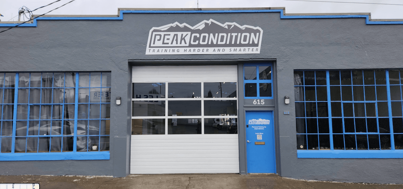 The Peak Condition studio at 615 SE Clay Street, Portland: grey building with a blue door and roll-up glass garage door