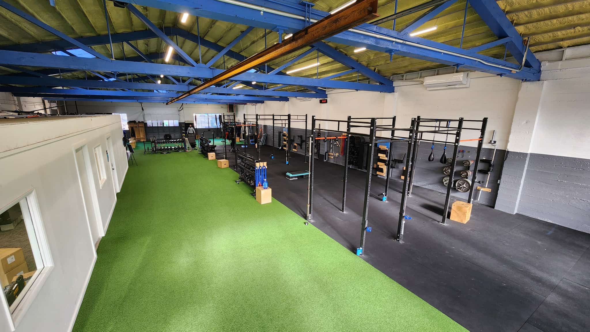 The Peak Condition training floor: blue roof trusses, green turf, and a wall of squat racks