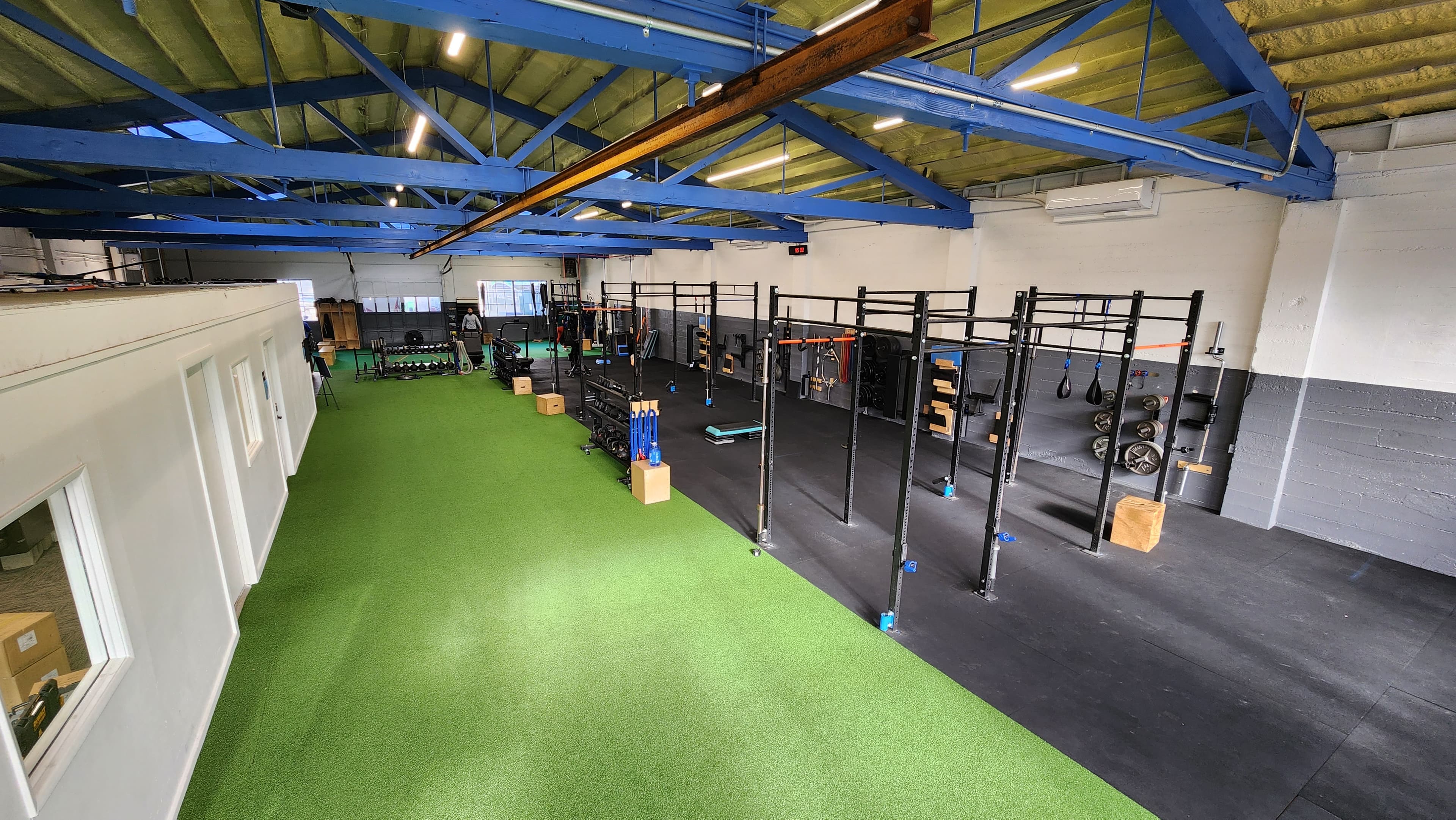 The Peak Condition training floor: blue roof trusses, green turf, and a wall of squat racks